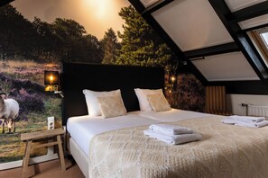 Un dormitorio con una cama grande, una mesita de noche, una lámpara de pared y un mural con una escena de bosque.