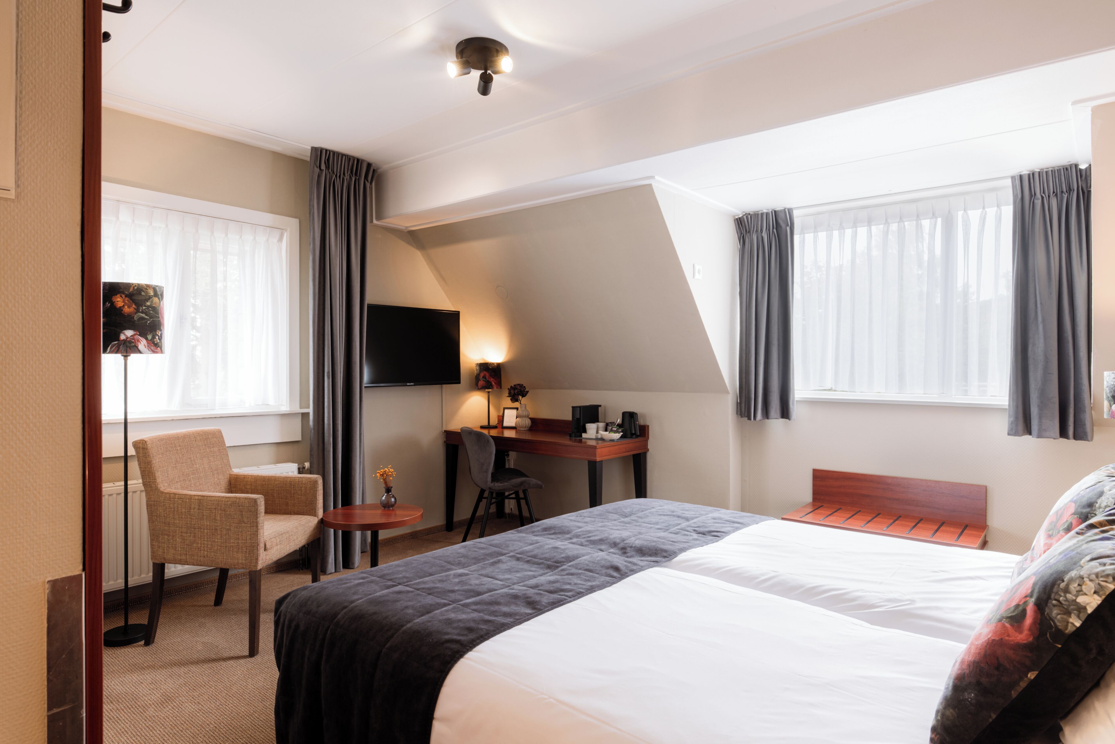 A hotel room with a bed, a desk, a chair, a television, and a window with curtains.