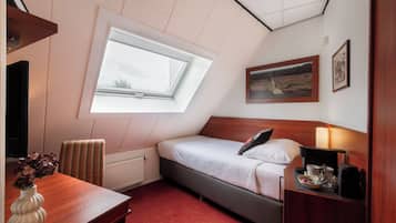 A bedroom with a skylight, a bed, a bedside table with a lamp, a chair, and a small table with a vase.