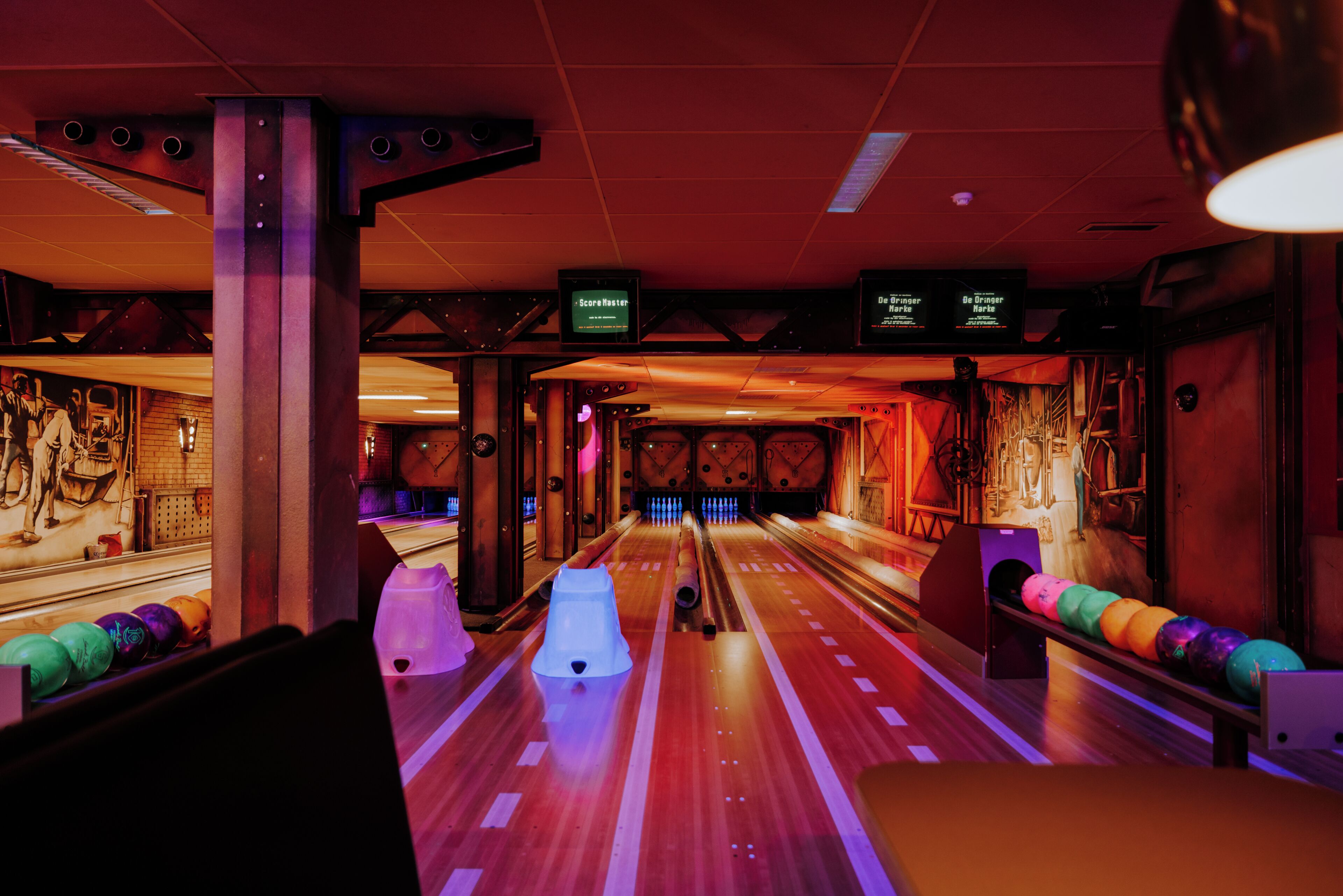 A bowling alley with multiple lanes, bowling pins, and a scoreboard.