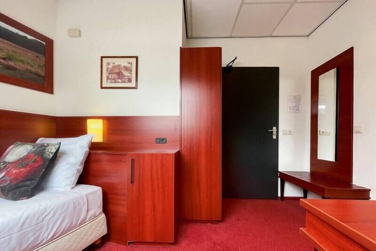 Una habitación de hotel con cama, escritorio, espejo y puerta.