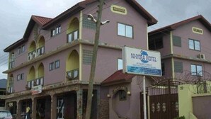 Un hotel a più piani con un cartello per NHYTRA HOTEL, caratterizzato da balconi e un ingresso chiuso da cancello.