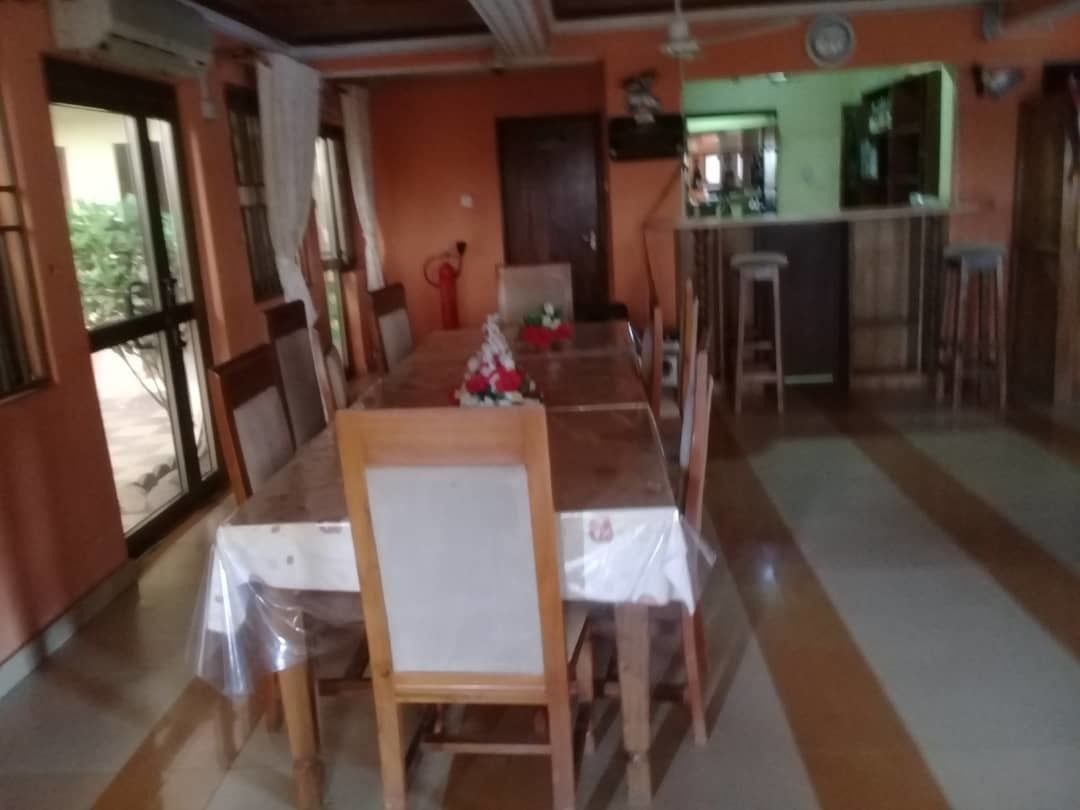 A dining area with a long wooden table, chairs, and a kitchen in the background.