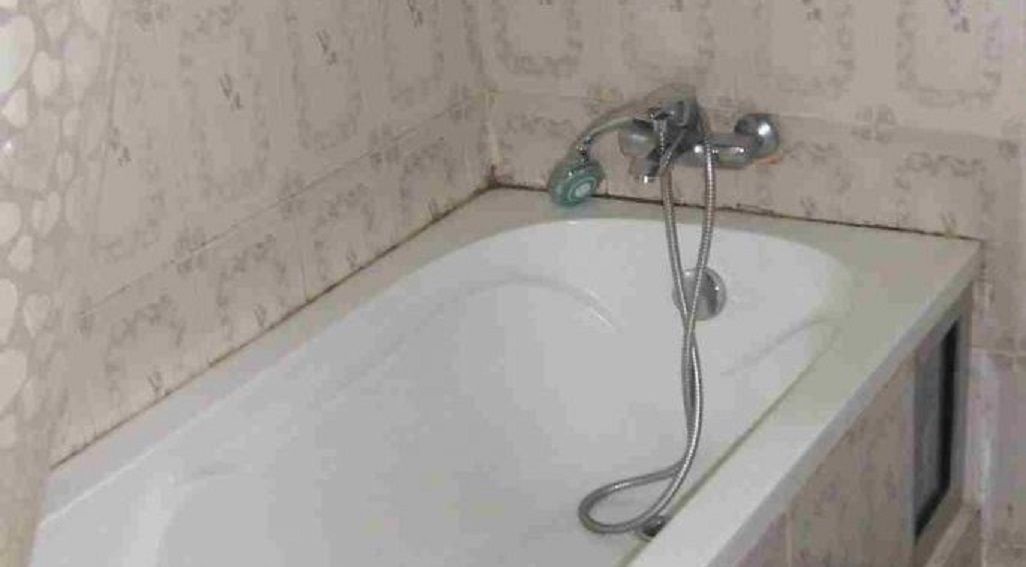 A bathtub with a handheld showerhead in a bathroom with patterned wallpaper.