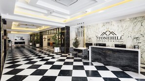 A hotel lobby with a checkered floor, a reception desk, and a marble wall with the hotel name. - Stonehill Suites (Bacolod)