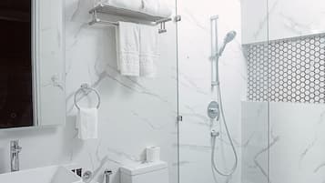 A modern bathroom with a marble wall, a glass shower enclosure, a white sink, and a toilet.