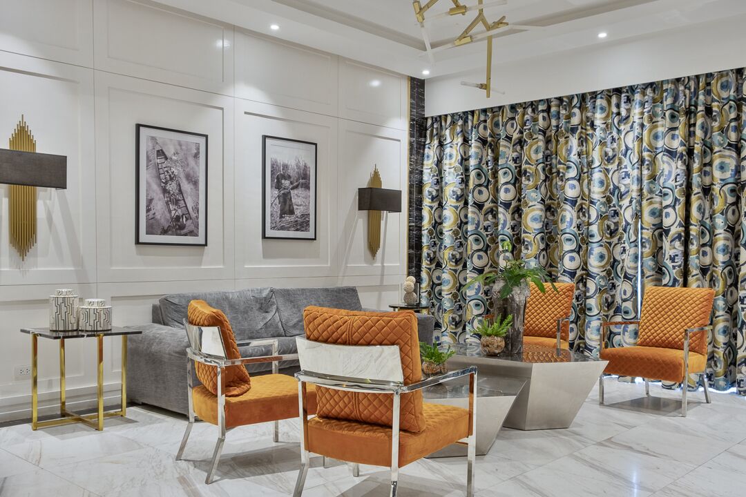 Een moderne woonkamer met een grijze bank, twee fauteuils, een glazen salontafel en een kamerbreed gordijn met een patroon.