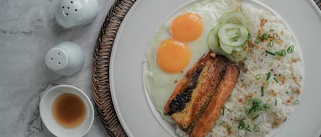 Un plato de huevos fritos, arroz y un trozo de pescado a la parrilla sobre un plato blanco.