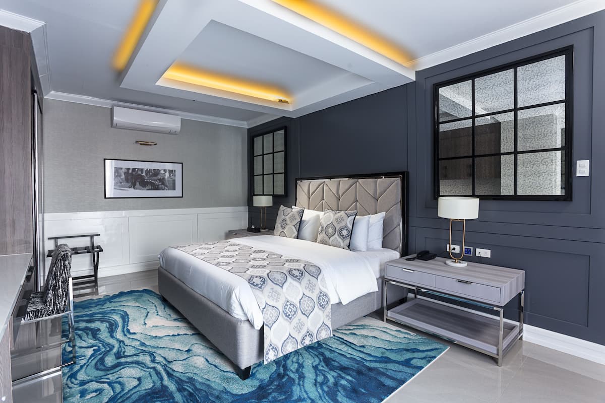 Un dormitorio moderno con una cama grande, mesitas de noche, un velador, un espejo y una ventana con vistas.