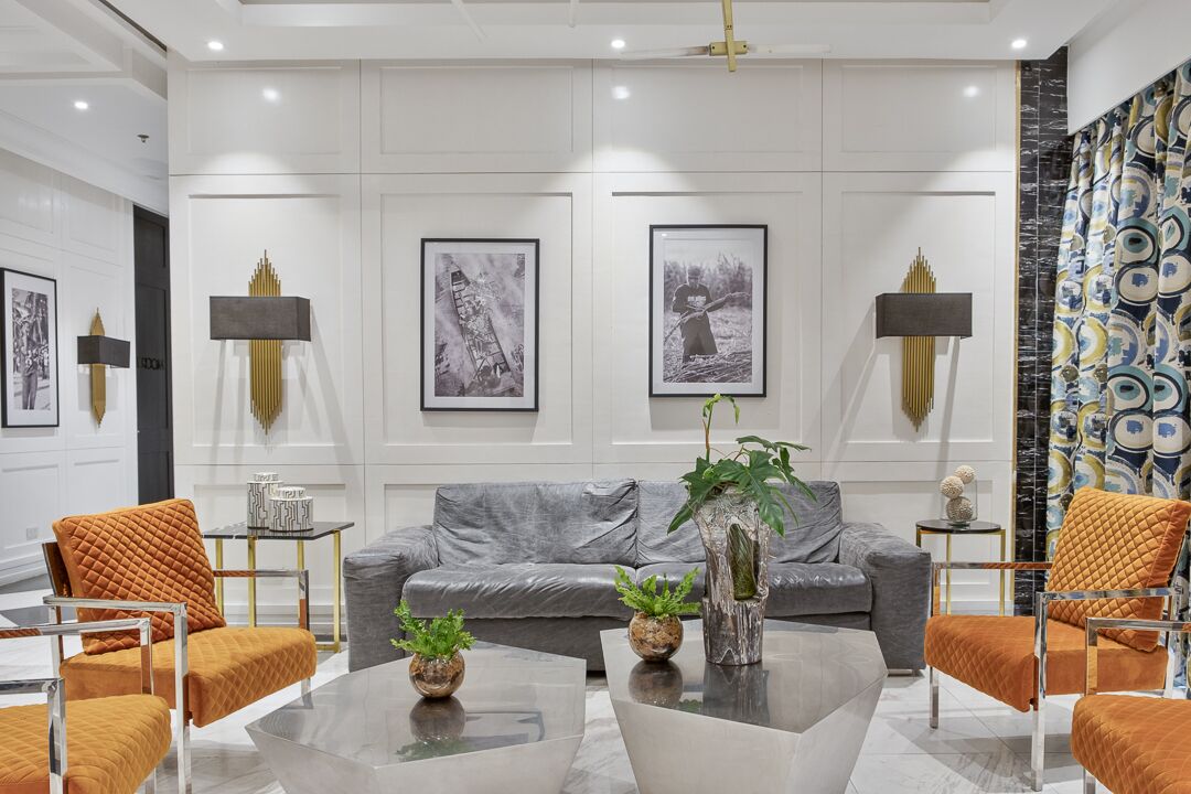A modern living room with a grey sofa, orange armchairs, a glass coffee table, and framed black-and-white photographs on the wall.