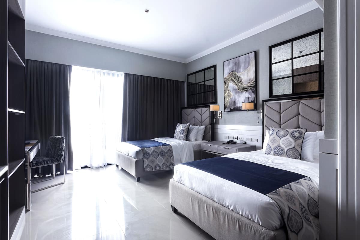 Habitación de hotel con dos camas, un escritorio, una silla y un ventanal grande.