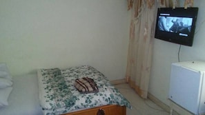 A small bedroom with a bed, a television mounted on the wall, and a white cabinet.