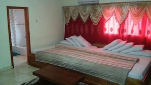 A bedroom with a bed, pillows, a bench, a door, and curtains. - New Mexico Hotel - Takoradi (Sekondi-Takoradi)