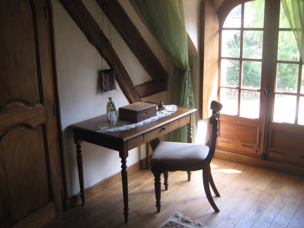 Une pièce avec un bureau en bois, une chaise, une fenêtre avec des rideaux et une vue sur la verdure.