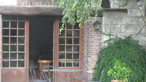 Een terras met een bakstenen vloer, metalen stoelen, een tafel en een potplant.