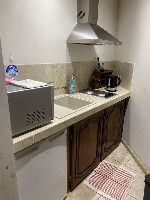 Una cocina con campana extractora de acero inoxidable, un lavamanos, un hervidor y una botella de jabón para lavar platos.