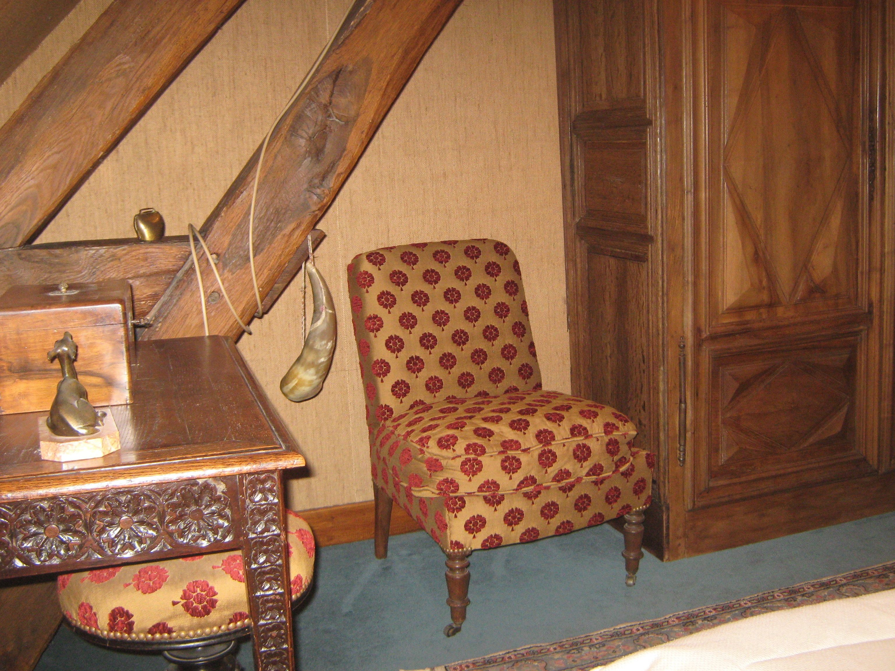 Una stanza con una scrivania in legno, una poltrona con motivo decorativo e un armadio in legno.