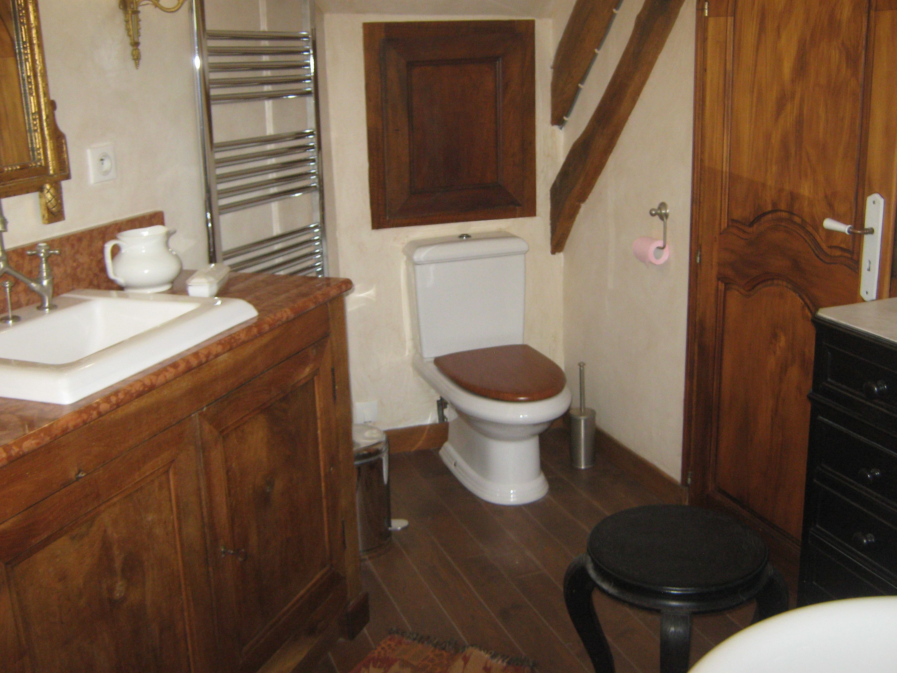 A bathroom with a wooden vanity, a toilet, and a black stool.