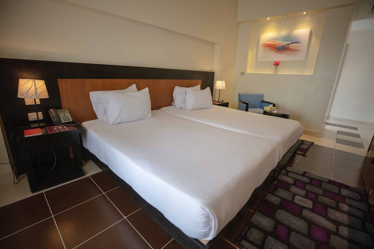 Ein Hotelzimmer mit einem großen Bett, zwei Nachttischen, einer Lampe, einem Telefon und einem Bild an der Wand.