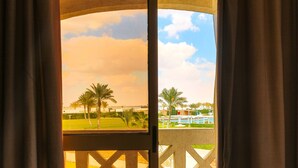 A room with a sliding glass door leading to a balcony with a view of palm trees and a swimming pool. - Mousa Coast (Ras Sudr)