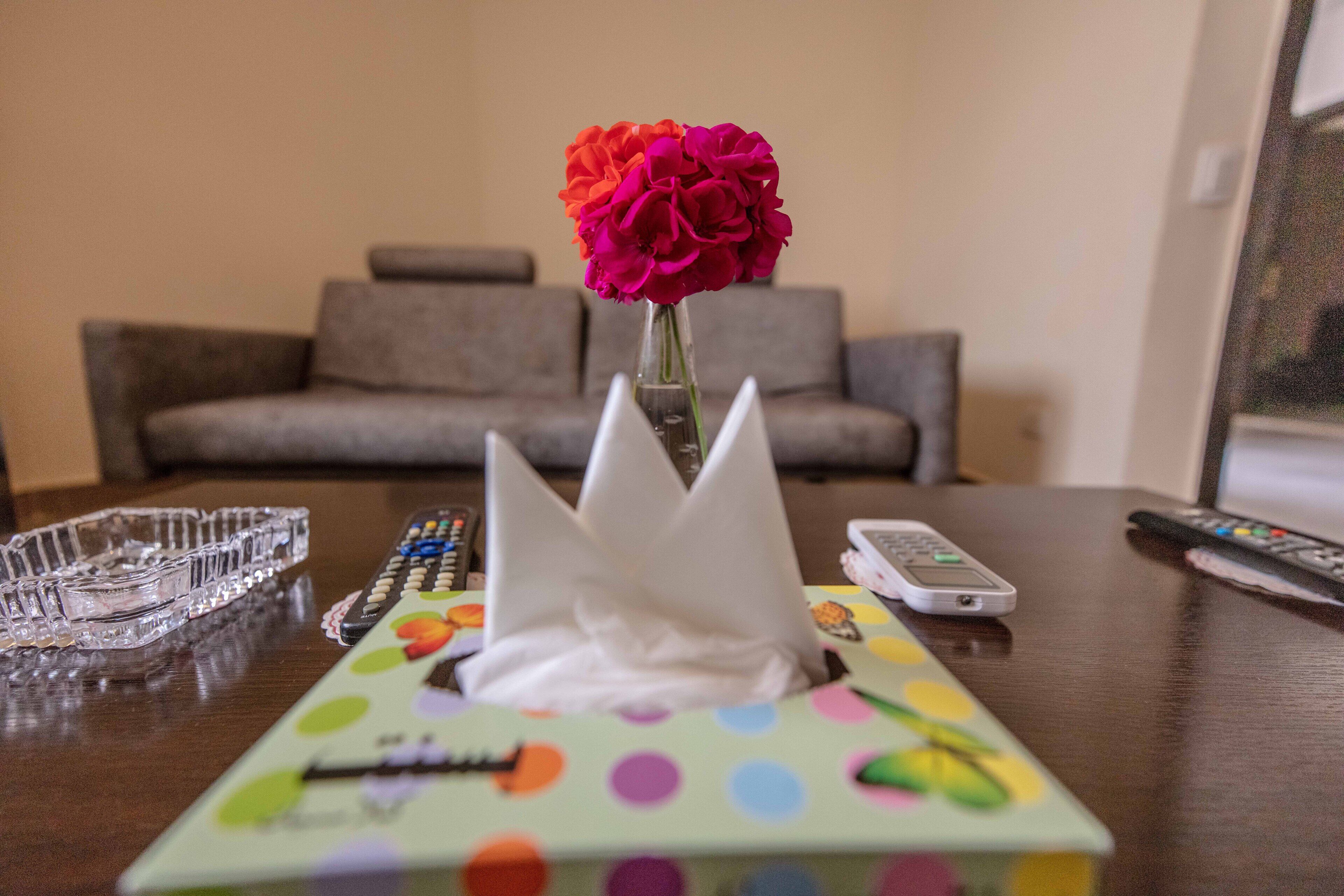 Una mesa con una caja de lunares, un florero con flores y controles remotos.