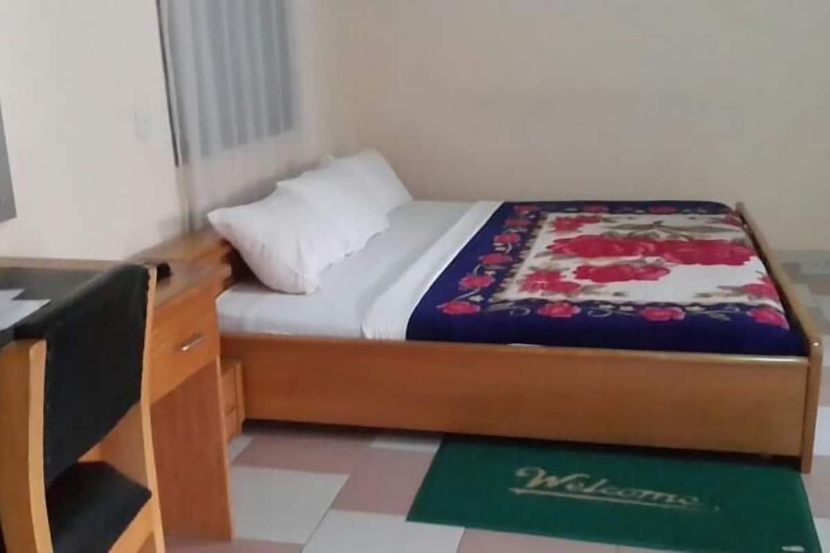 Un llit individual amb llençols florals, una tauleta de nit i una cadira.