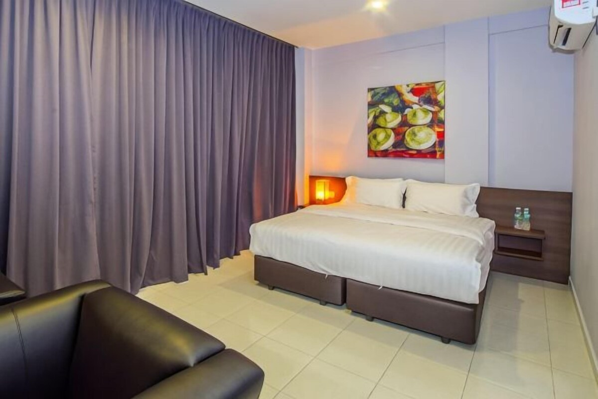 Habitación de hotel con cama, mesita de noche, lámpara, un cuadro en la pared y cortina.