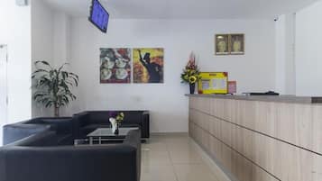 Un área de recepción con sofá, una mesa de centro, televisor y mostrador de recepción.