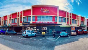 A hotel with a red facade, multiple shops on the ground floor, and several cars parked in front. - Hotel Seri Rembau (Rembau)