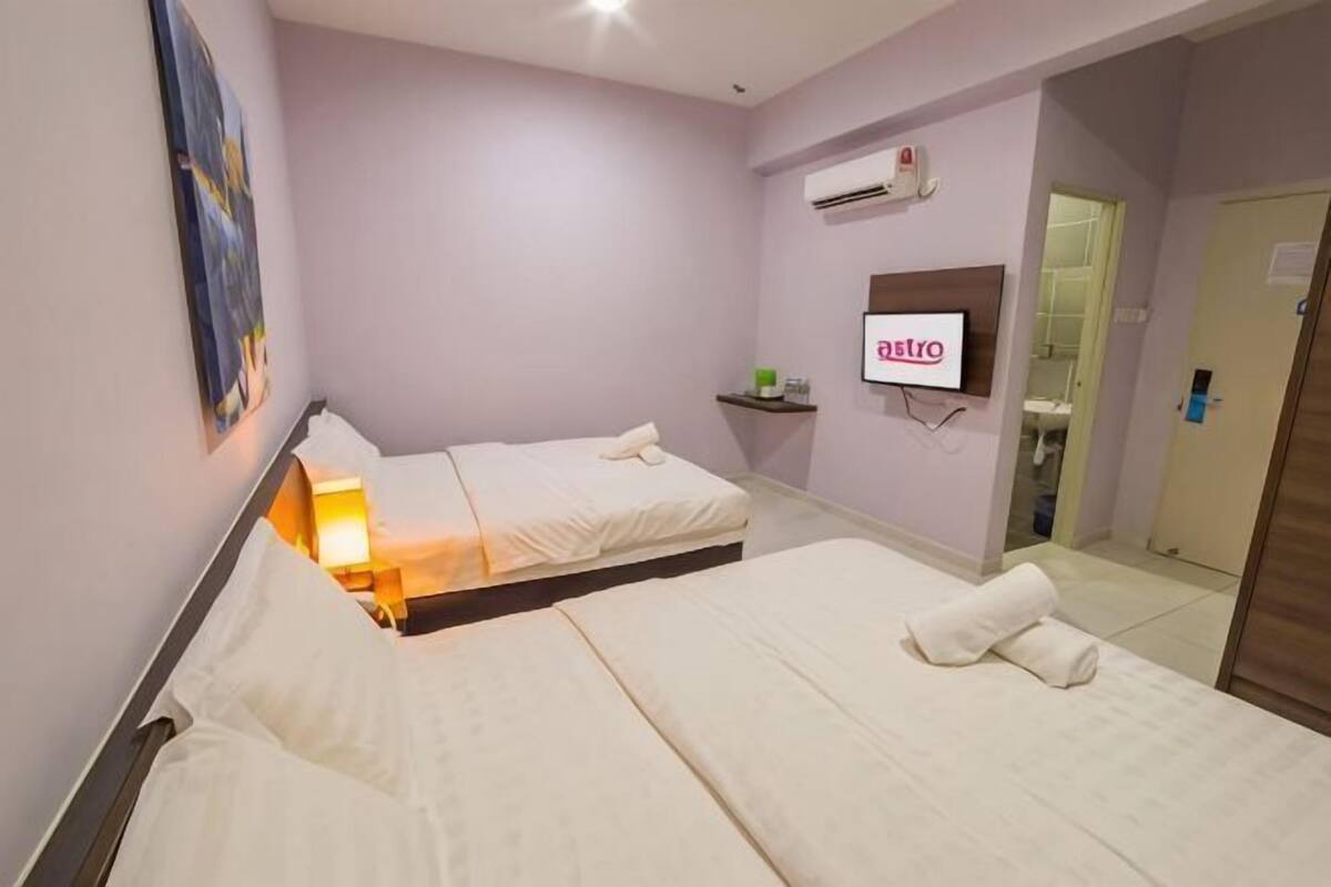 A hotel room with two beds, a TV, an air conditioning unit, and a bathroom visible through an open door.