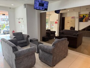 Un hall con sofás grises, una mesa de centro y un televisor montado en la pared.