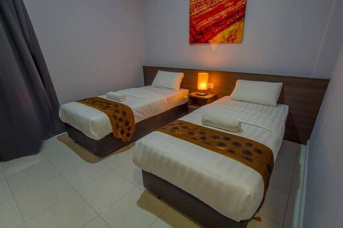 A hotel room with two single beds, a nightstand with a lamp, and a red abstract painting on the wall.