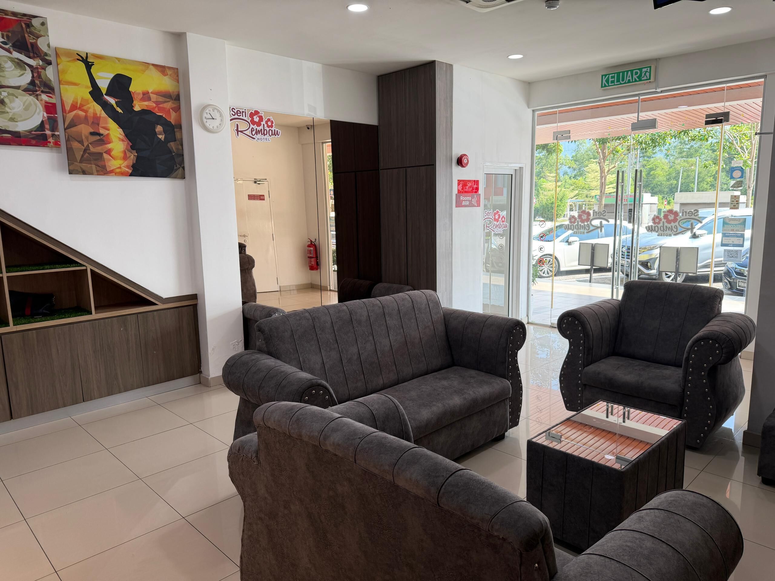 A hotel lobby with grey sofas, a wooden bench, and a glass door leading outside.