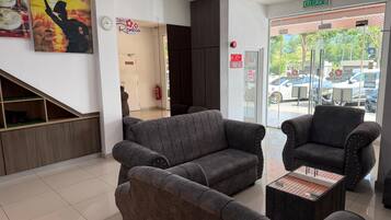 A hotel lobby with grey sofas, a wooden bench, and a glass door leading outside.