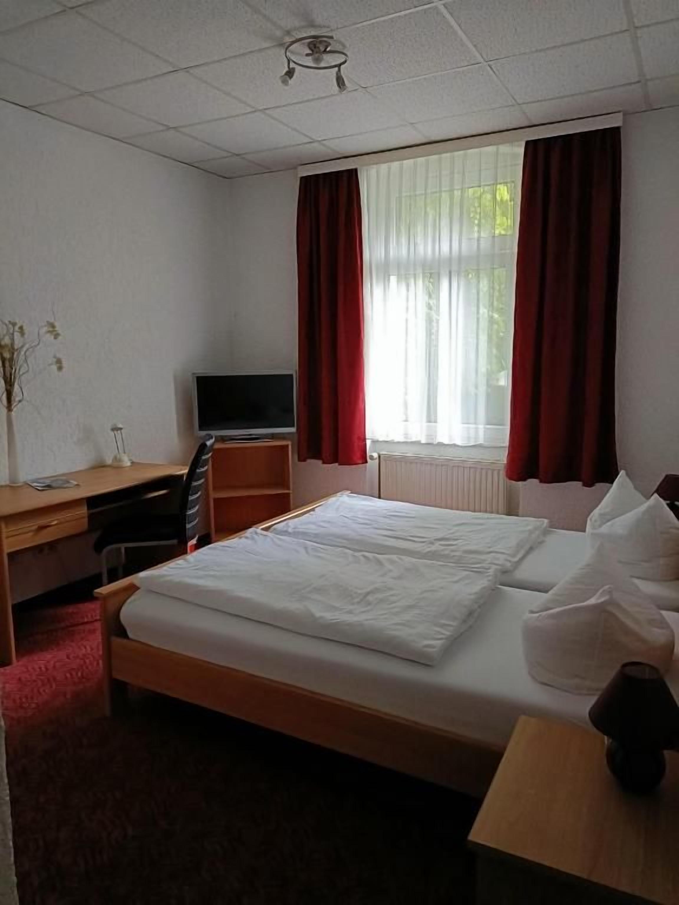 Hotellihuone, jossa on sänky, työpöytä, televisio ja ikkuna, jossa on verhot.