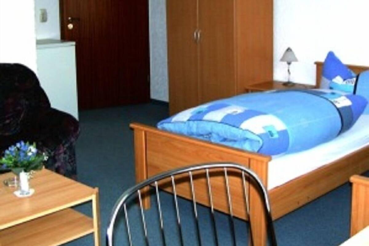 Une chambre à coucher avec un lit en bois, une chaise, une petite table et une armoire.