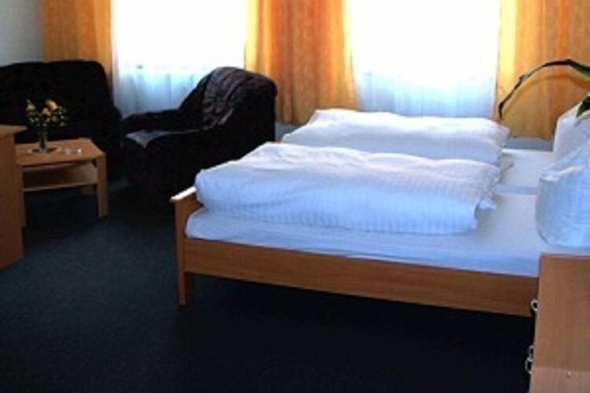 Une chambre d’hôtel avec un lit en bois, une chaise, une table de chevet et une fenêtre avec des rideaux.