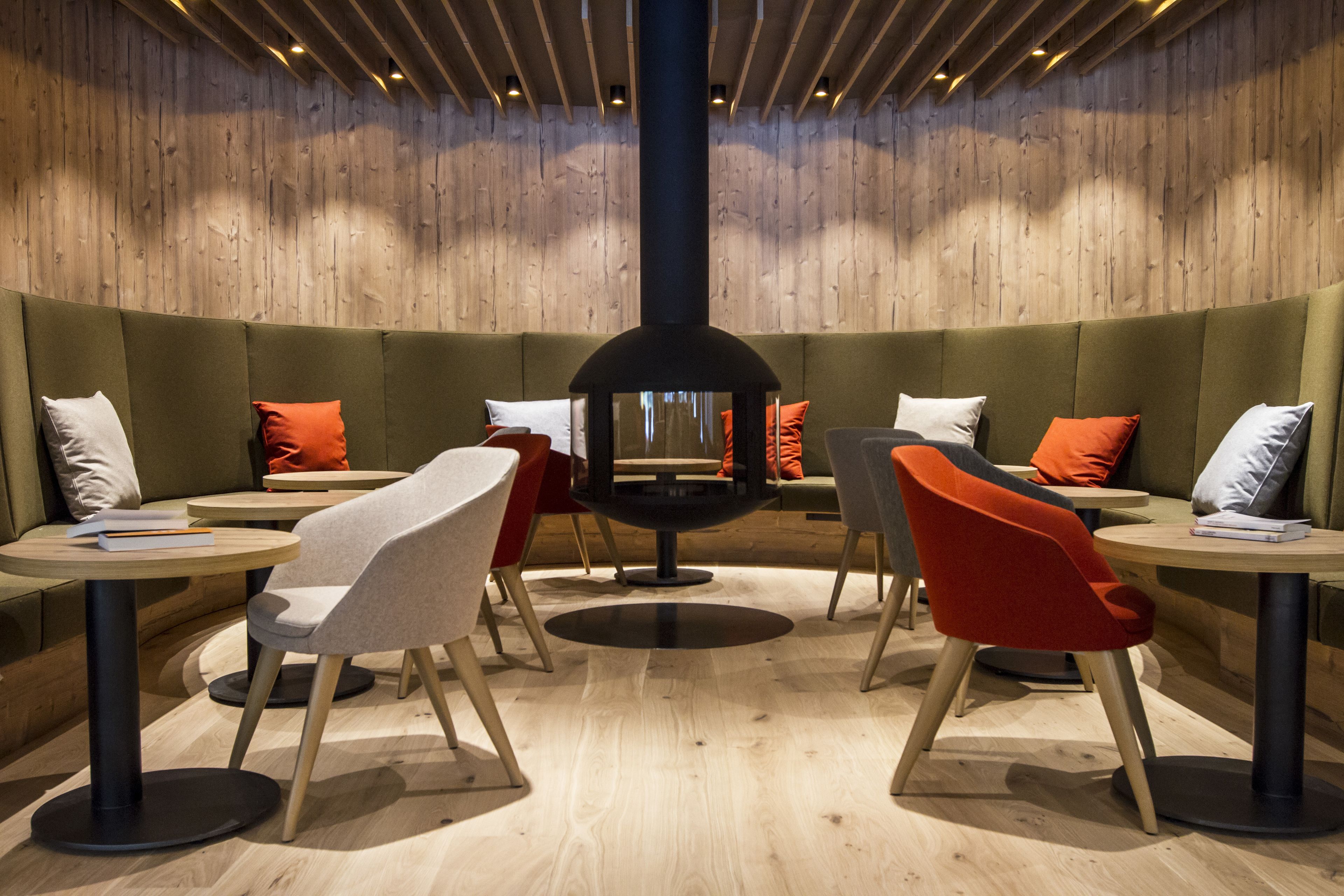 Un'area lounge moderna con una disposizione circolare di posti a sedere al centro, pareti in legno e diversi tavoli e sedie.