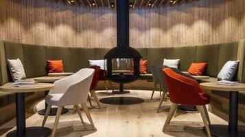 Un'area lounge moderna con una disposizione circolare di posti a sedere al centro, pareti in legno e diversi tavoli e sedie.
