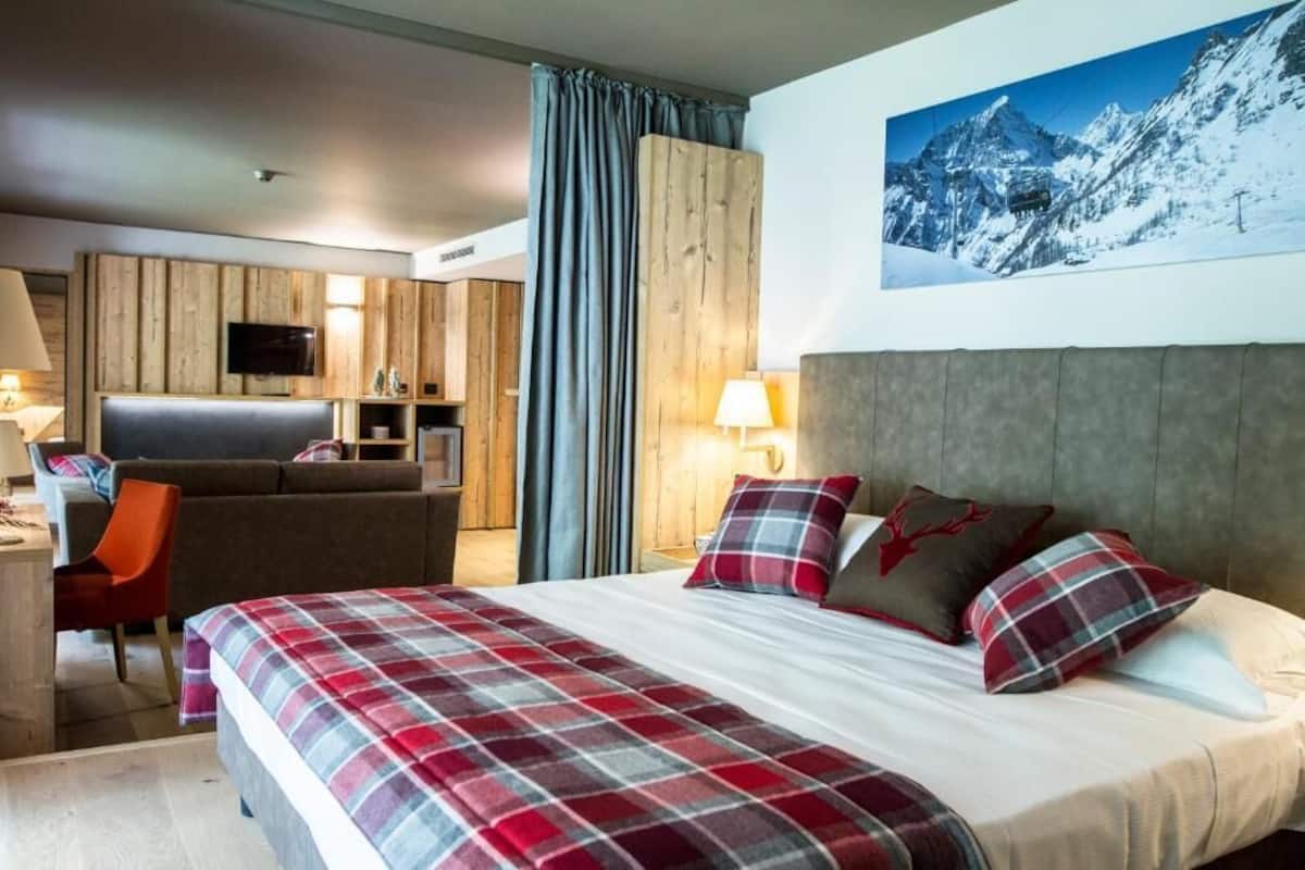 A hotel room with a bed, a desk, a chair, a television, and a mountain view.
