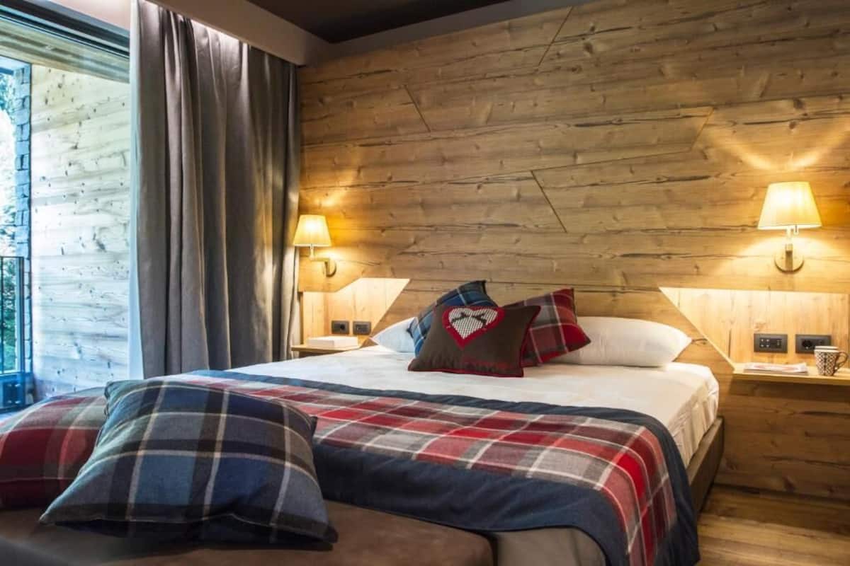 A cozy hotel room with a wooden headboard, a plaid bedspread, and two bedside lamps.