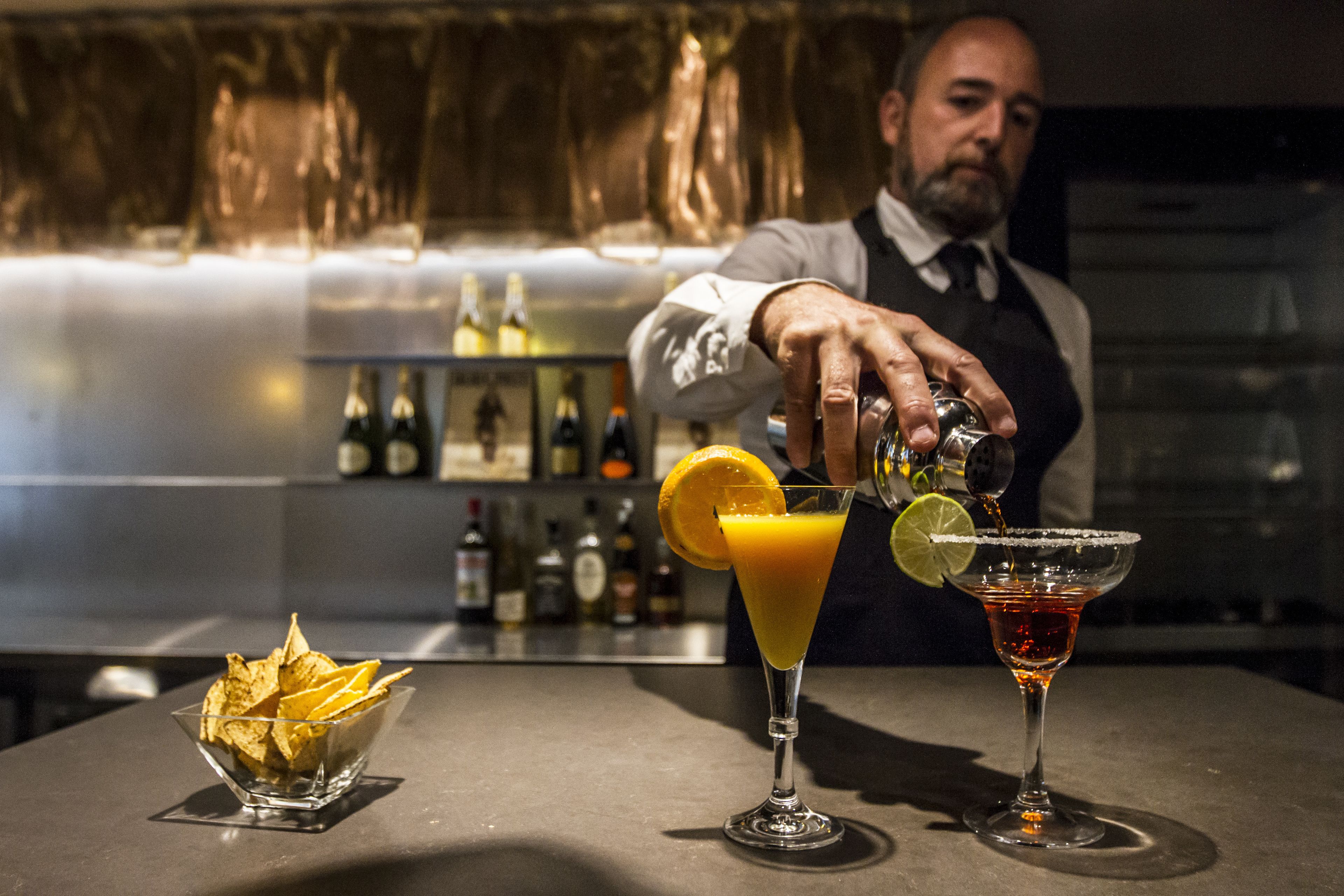 Eine Bar mit einem Barkeeper, der Getränke zubereitet, einer Schüssel Chips und einer Theke voller Flaschen.