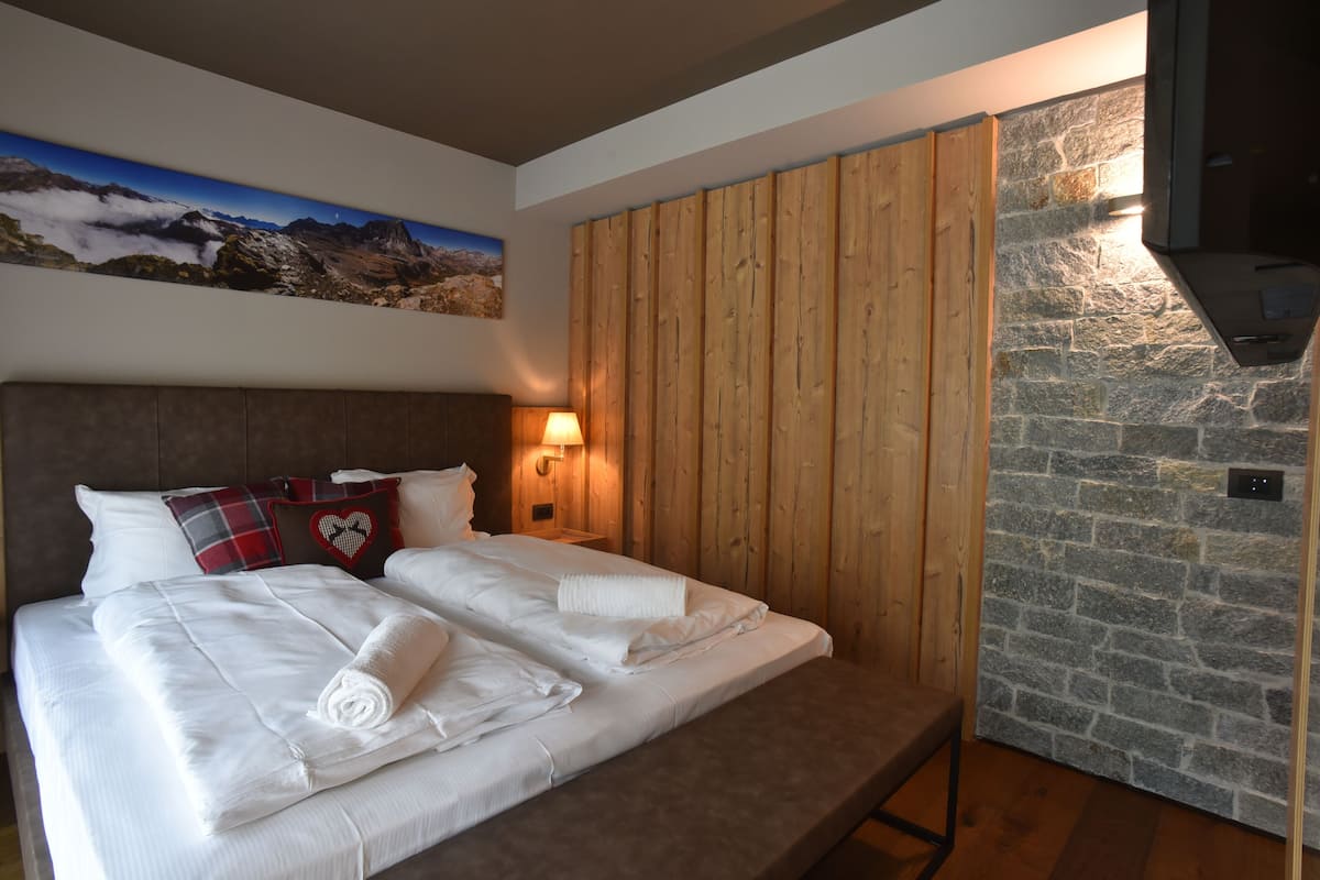 A hotel room with a bed, wooden panel wall, stone wall, and a mounted TV.