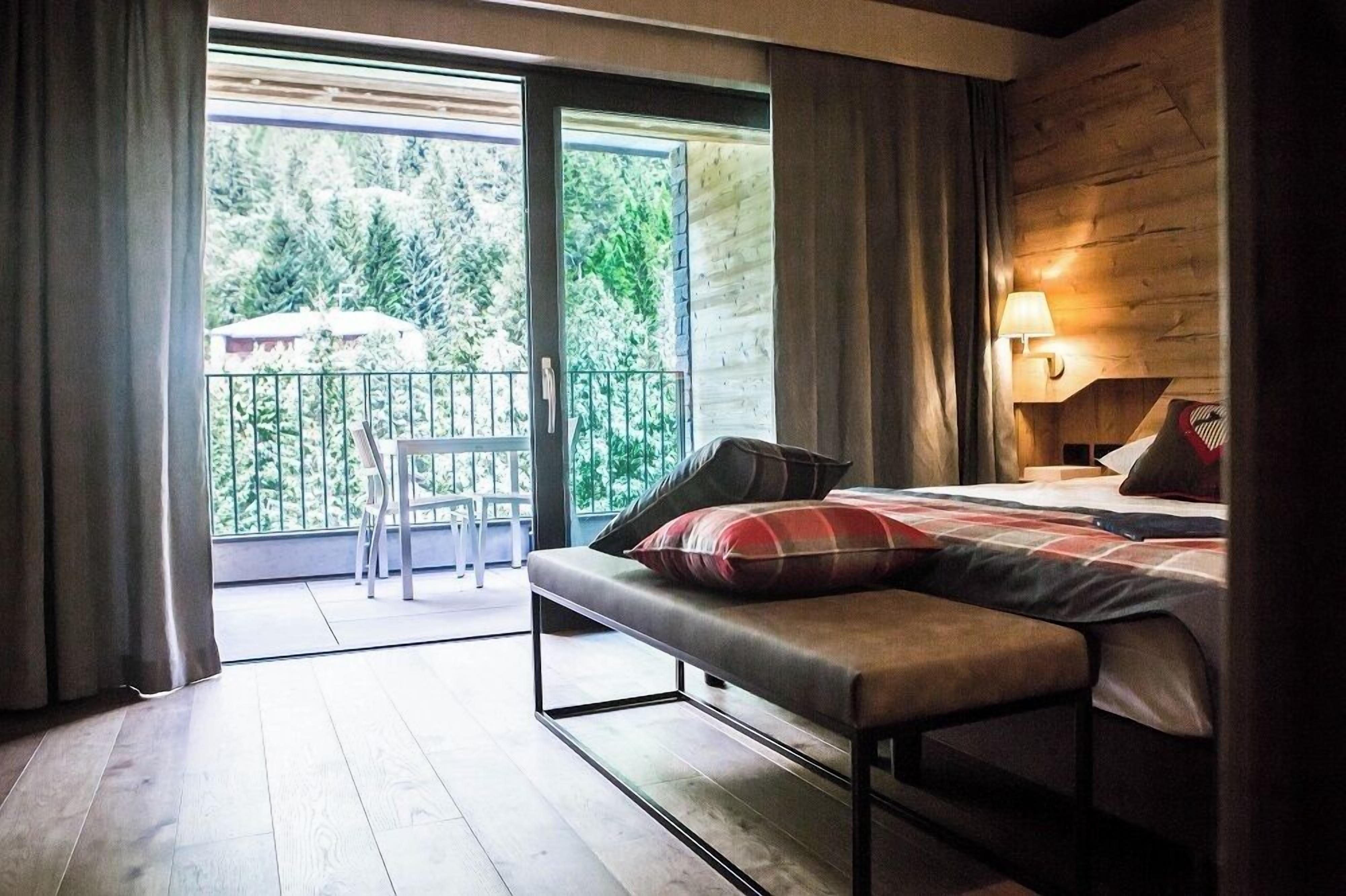 A bedroom with a bed, bench, and a balcony with a chair.