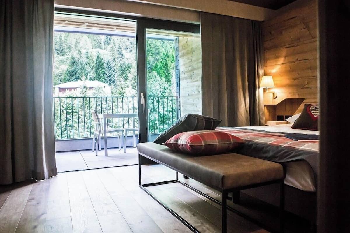 A bedroom with a bed, bench, and a balcony with a chair.
