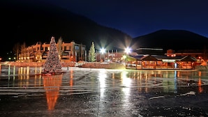 A nighttime view of a town with a large illuminated Christmas tree in the foreground, reflecting on a frozen body of water. - Edgewater 1448 (Keystone)