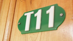 Vihreä kyltti, jossa on valkoisilla kirjaimilla teksti ”T11”, ja se on kiinnitetty puupintaan.