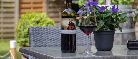 A bottle of wine, a glass of red wine, and a potted plant on an outdoor table.