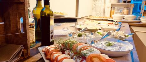 Una mesa de buffet con diversos platos, incluyendo un aperitivo de tomates y queso en una fuente, y botellas de vino.