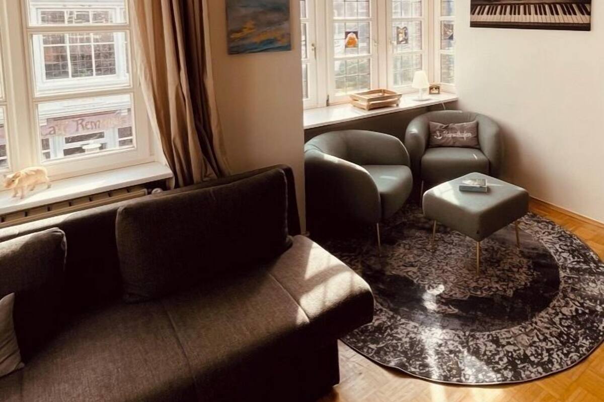 A living room with a sofa, armchairs, a coffee table, a piano, and a chandelier.